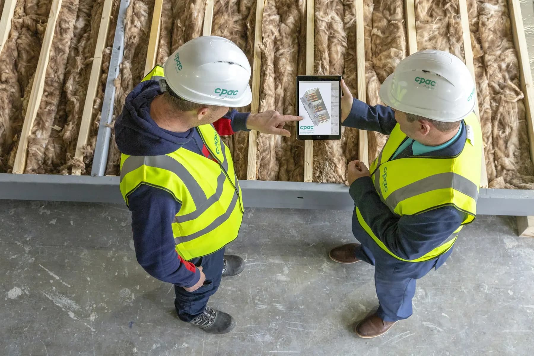 Two construction workers in hard hats reviewing plans on a tablet
