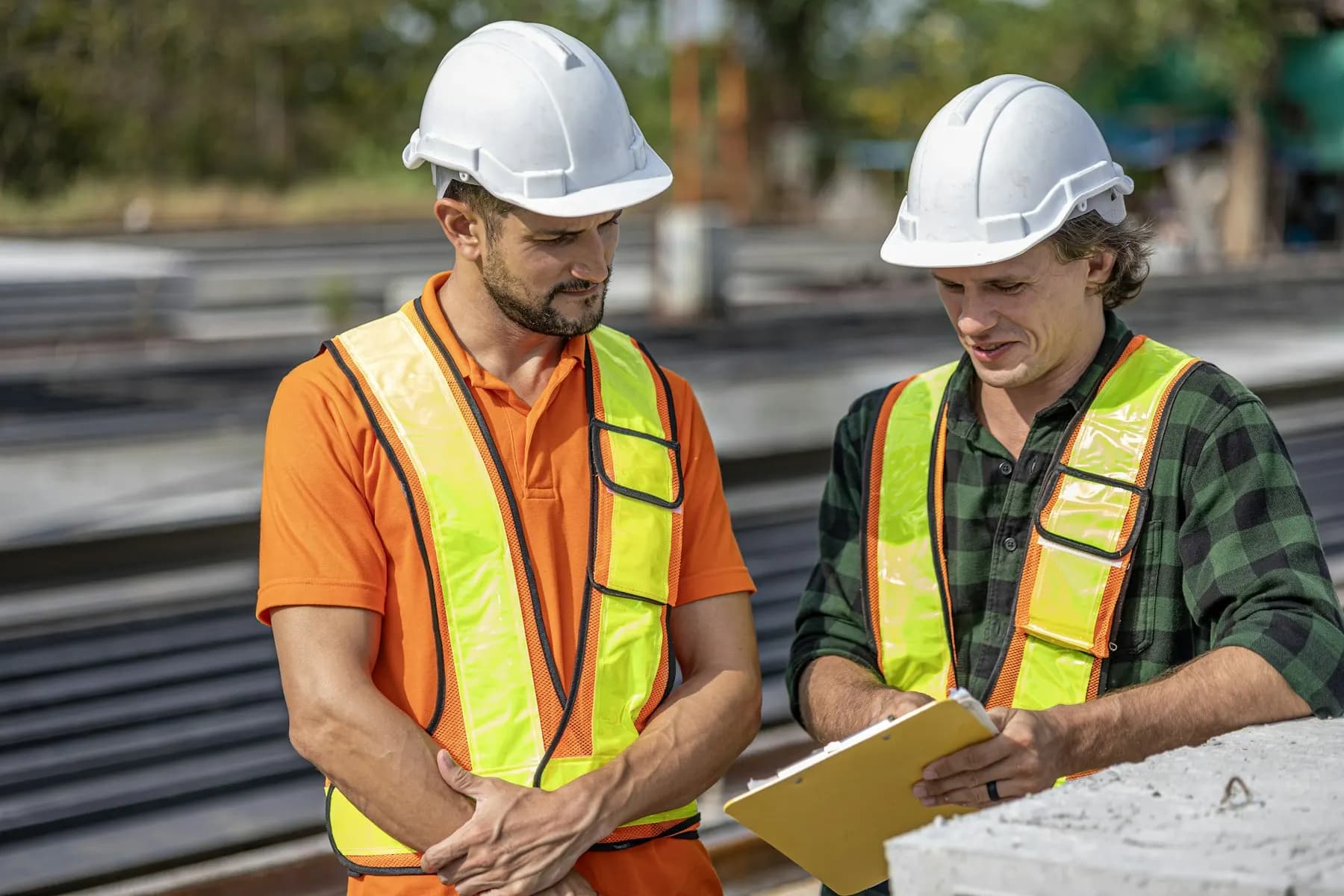 Two construction workers in hard hats and hi-vis vests reviewing plans on site