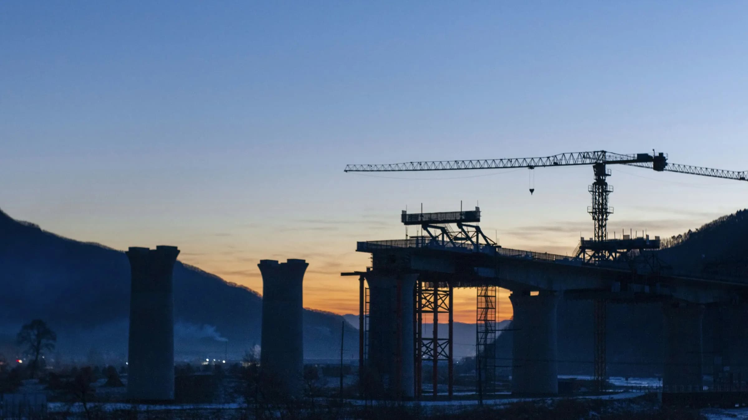 Cranes and bridge piers rising over the water at dusk
